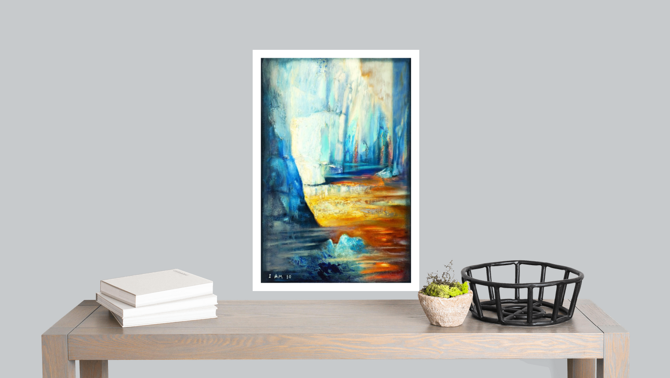 Framed abstract painting on a table with books and a basket against a gray wall