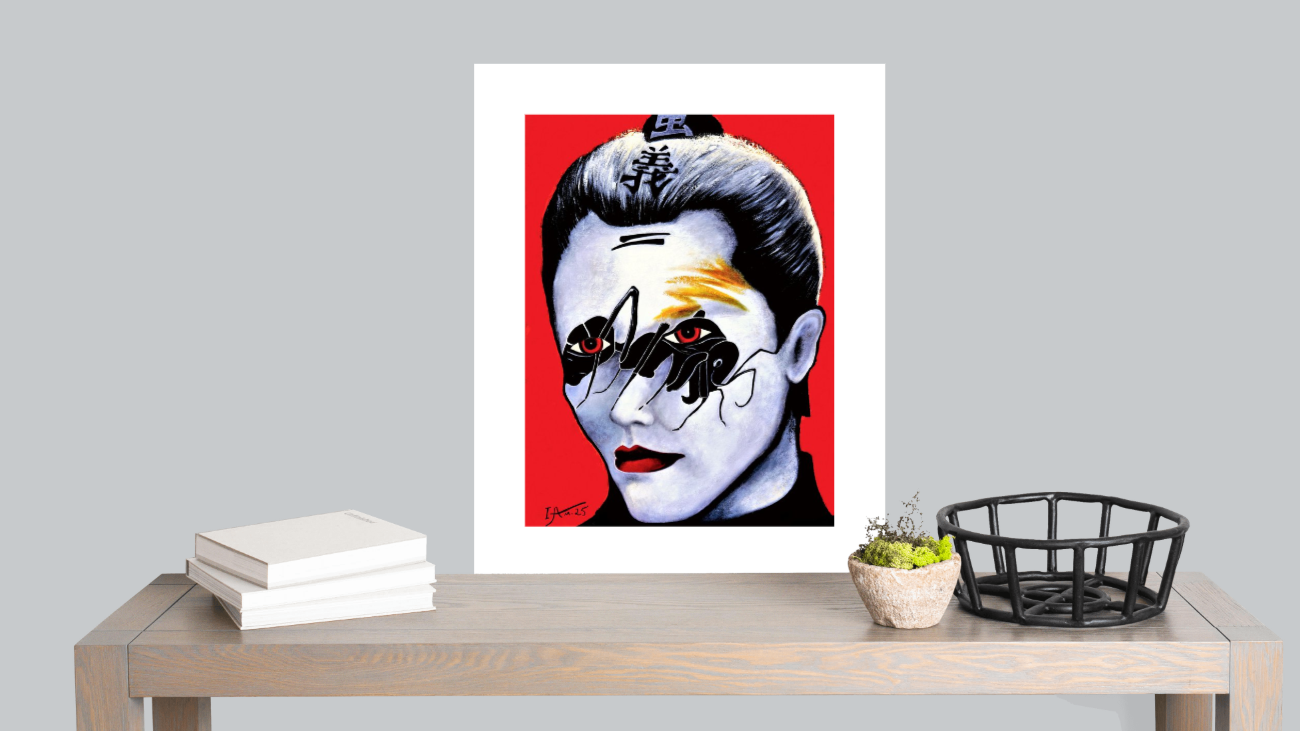 Framed artwork of a stylized face on a red background, displayed on a table with books and a plant.