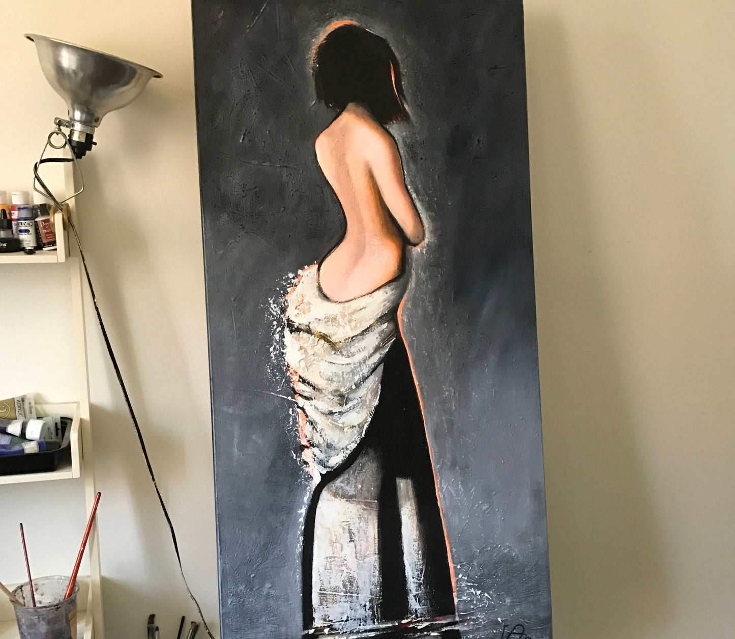 Large painting of a nude figure on a dark background in an art studio.