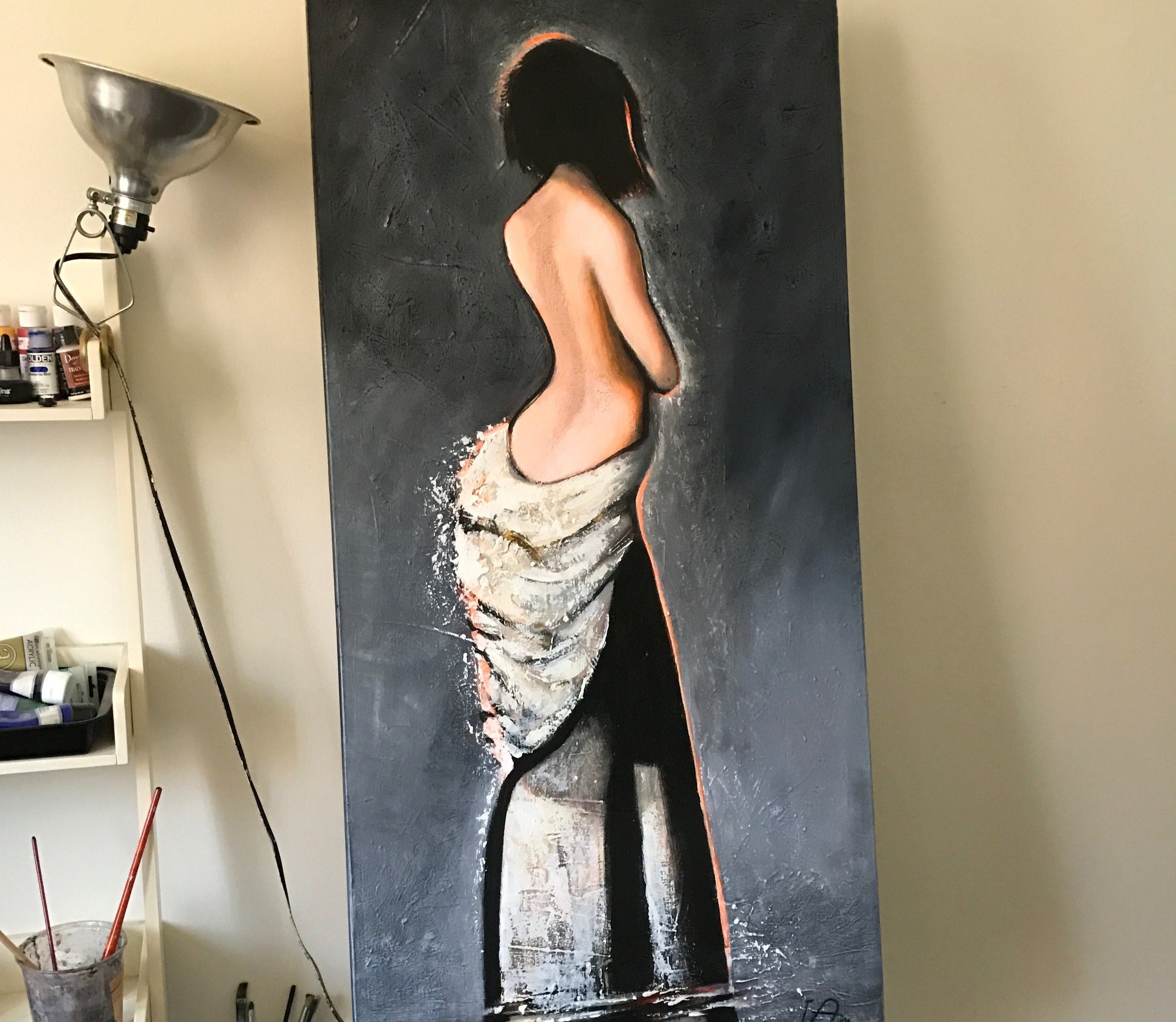Large painting of a nude figure on a dark background in an art studio.